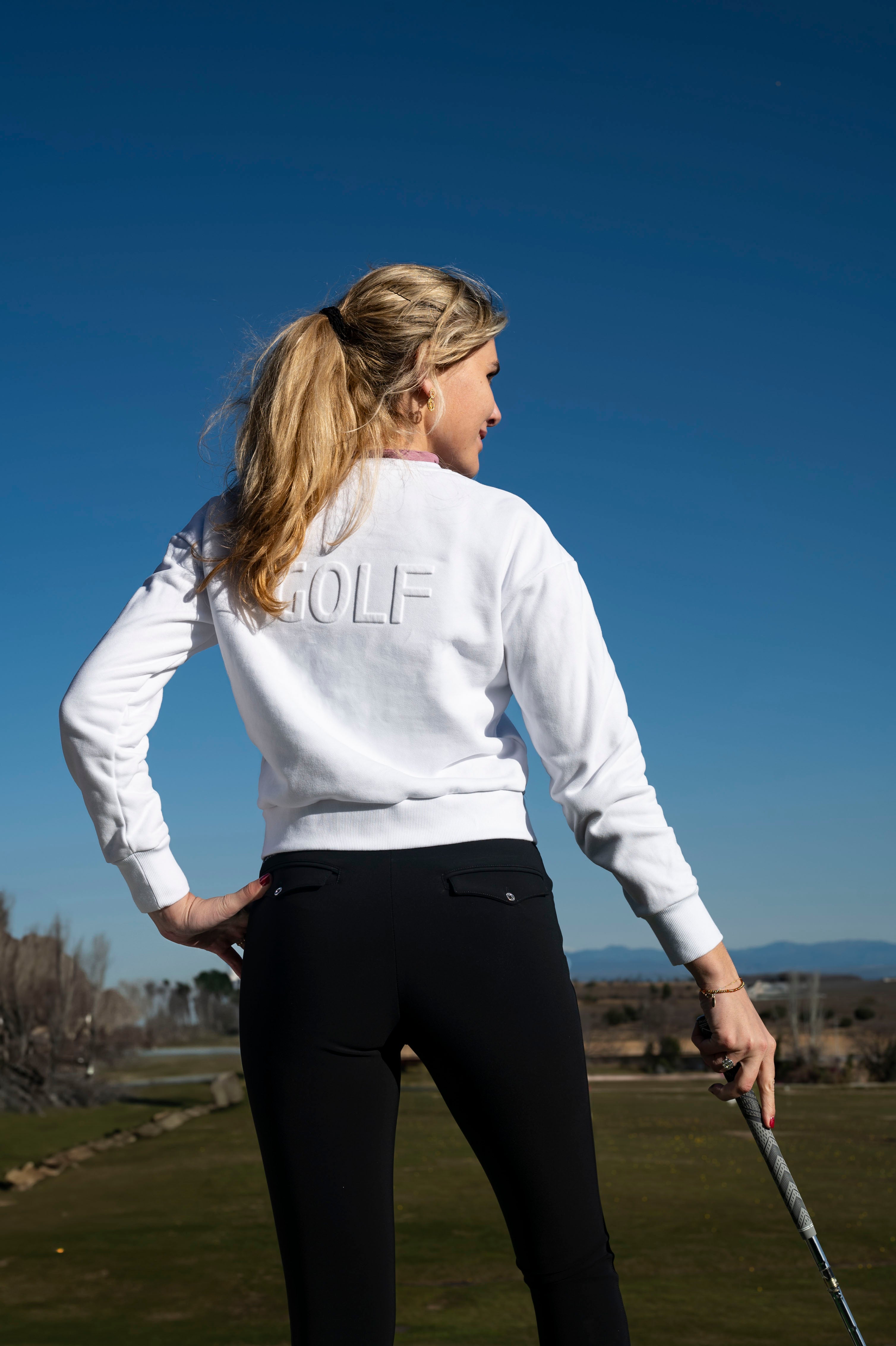 Golfer wearing white Flairway golf sweater with embossed GOLF logo on the back, and high-waisted golf pants