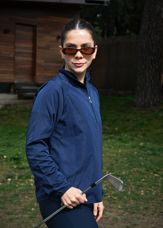Person in a blue jacket holding a golf club outdoors with a wooden cabin in the background