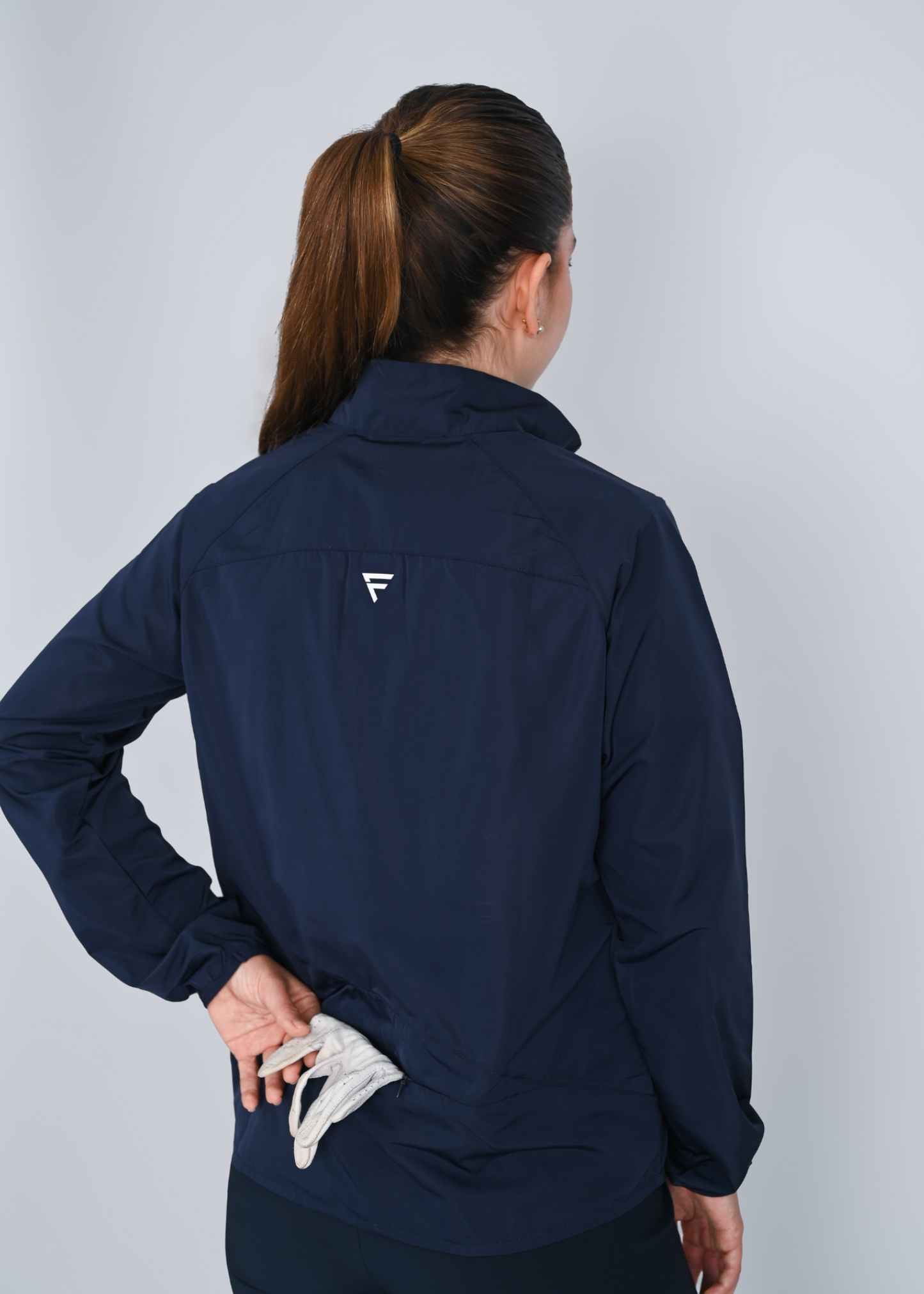 Person wearing a navy blue jacket with a logo on the back against a light gray background