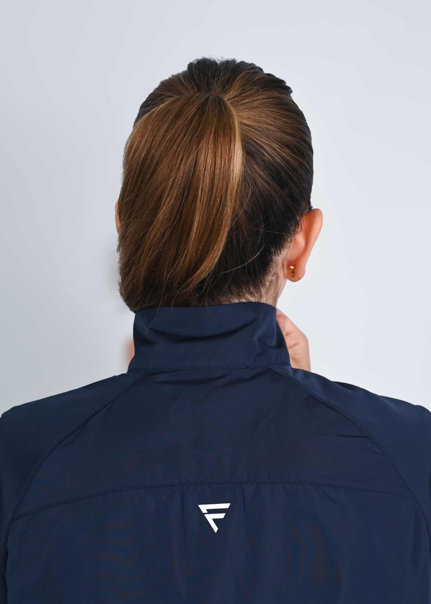 Person wearing a navy jacket with a brand logo on a light gray background