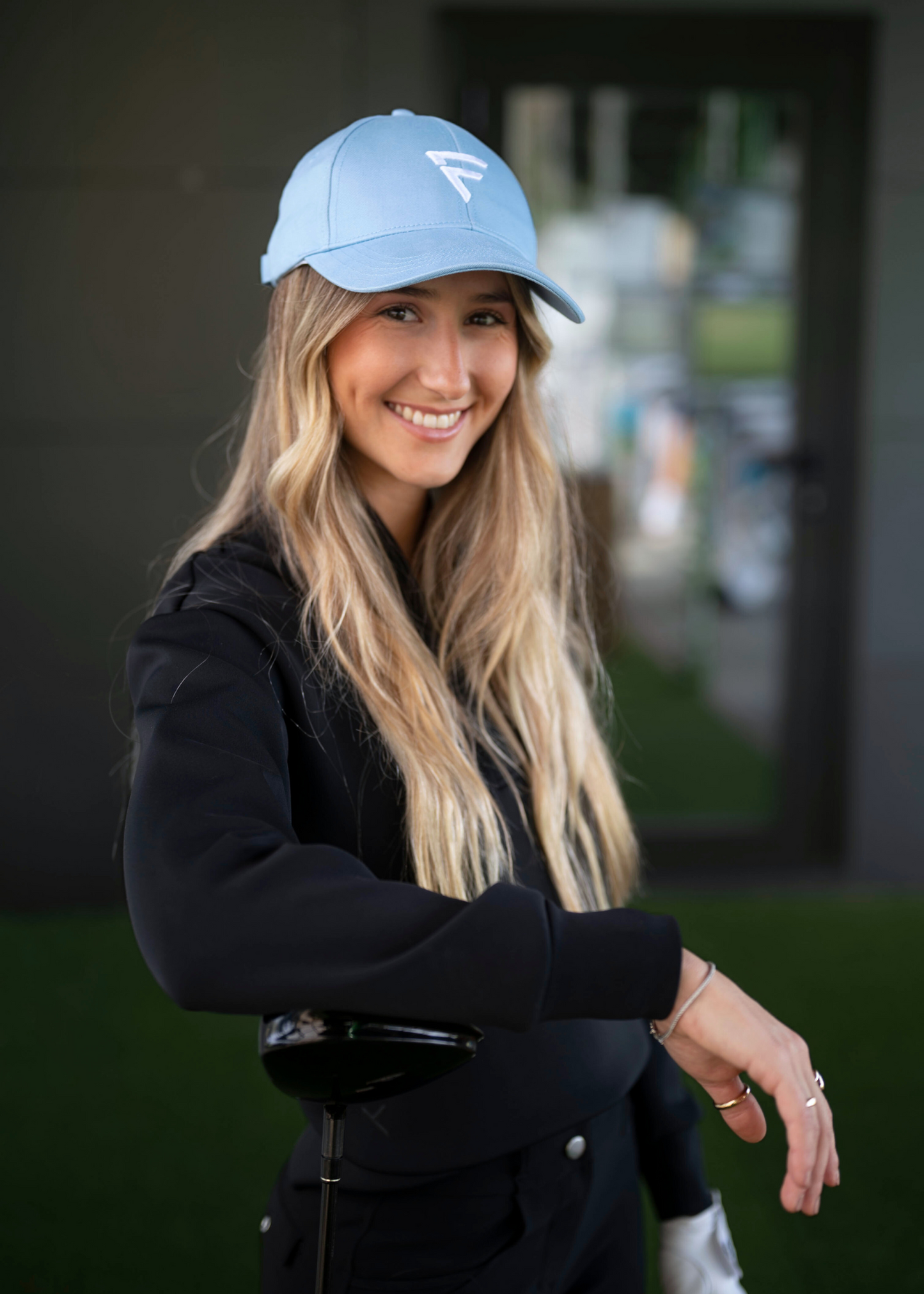 A person wearing a stormy blue golf cap with a visible letter 'F' on it, standing outdoors.