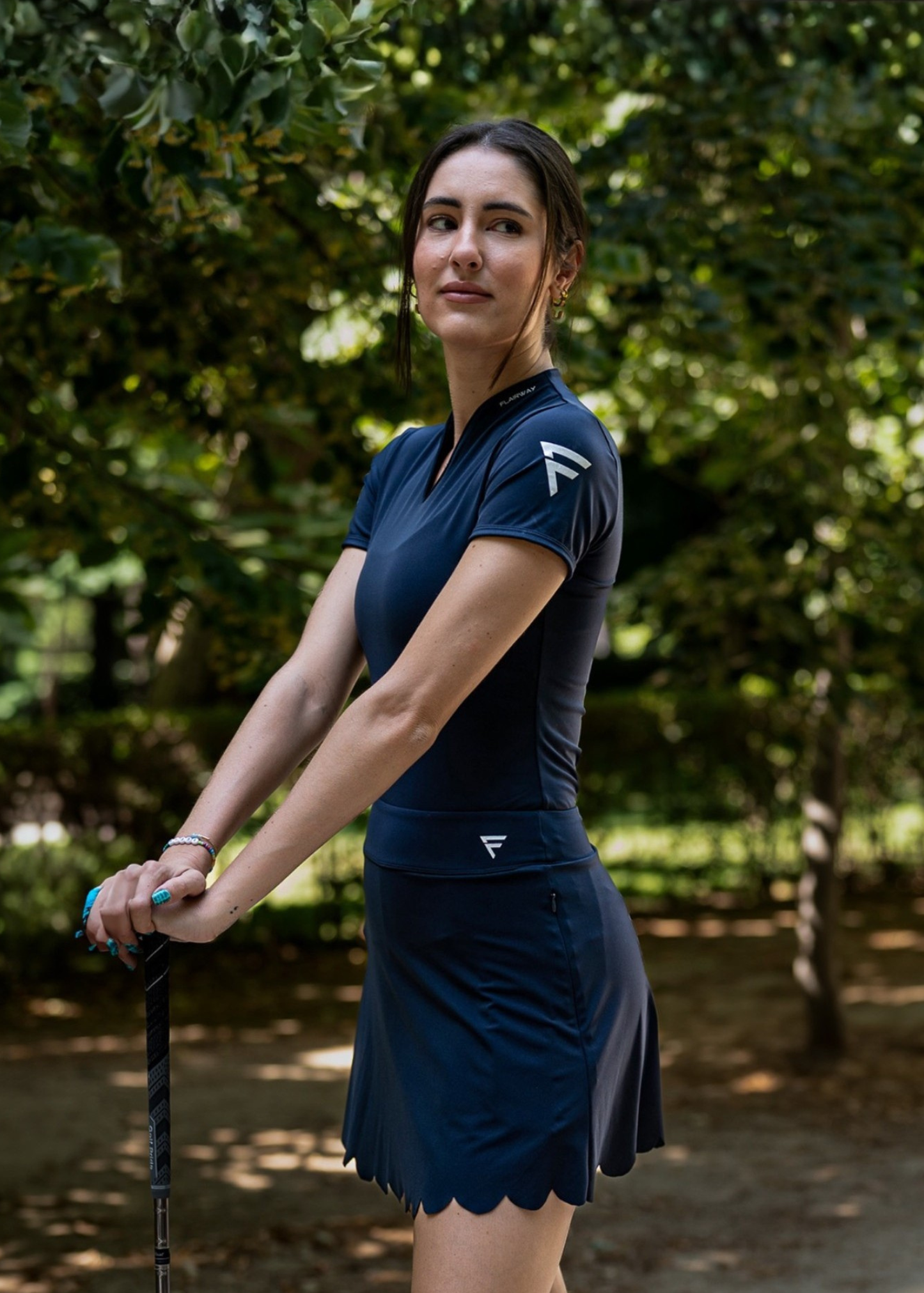 Woman in a navy blue golf outfit holding a club outdoors.