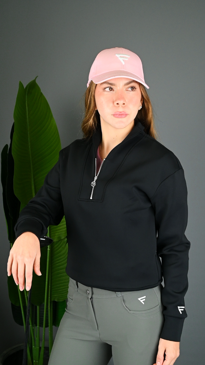 Person wearing a black jacket and gray pants with a pink cap, standing against a dark background.