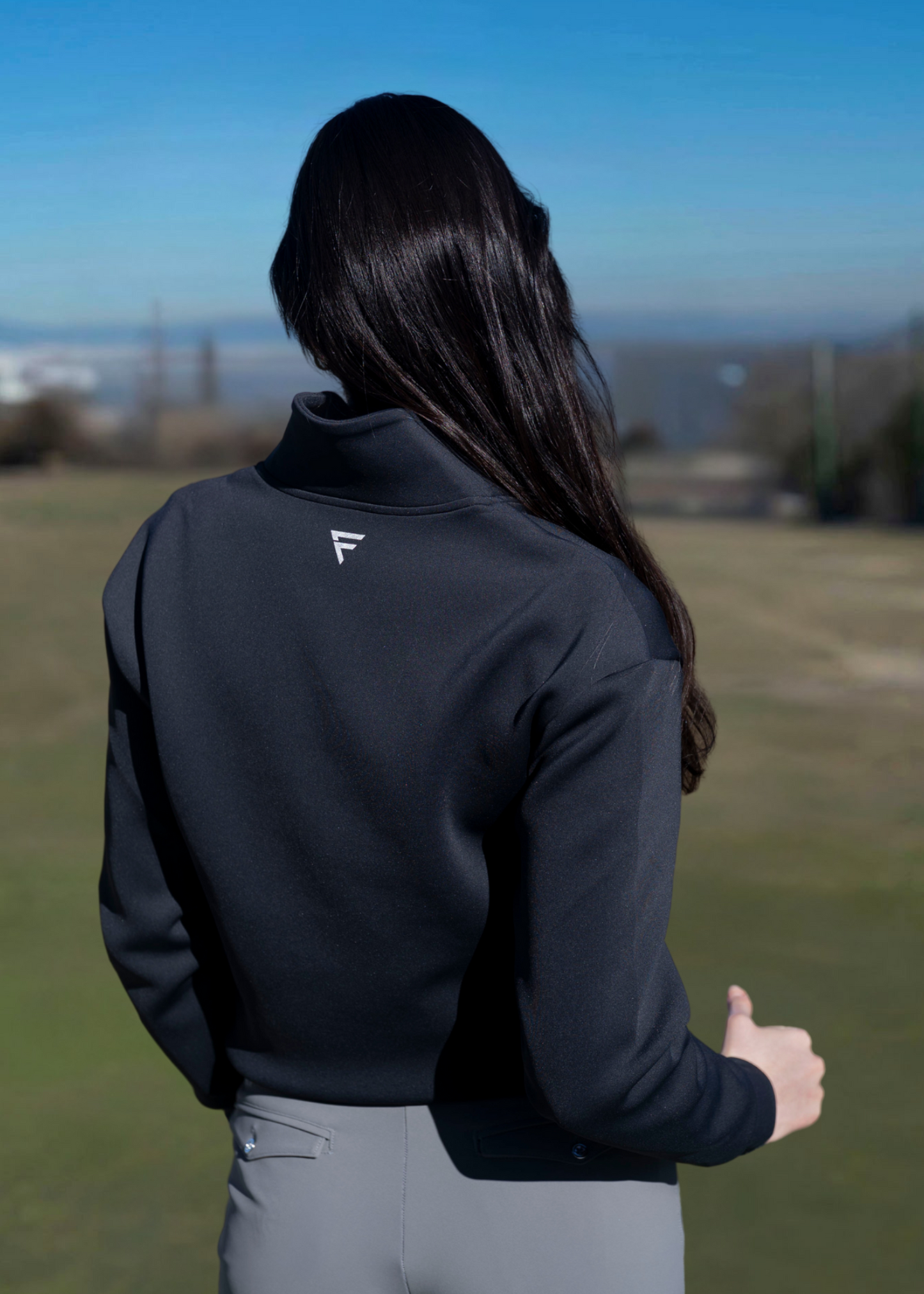 A woman wearing a navy-colored sweater with an athletic fit, featuring a quarter-zip design and a collar. The sweater is styled for golfing with a subtle logo on the side.