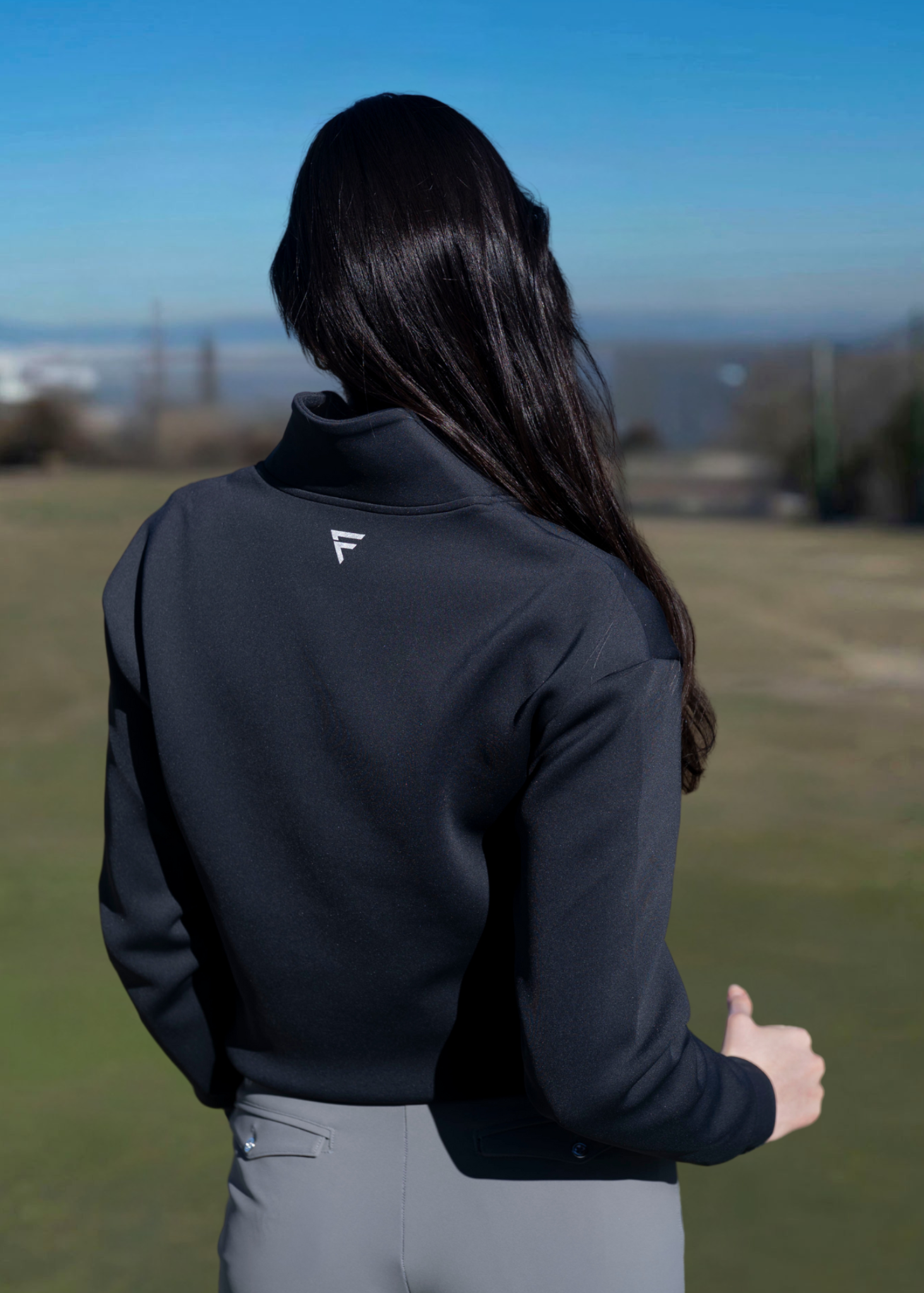 A woman wearing a navy-colored sweater with an athletic fit, featuring a quarter-zip design and a collar. The sweater is styled for golfing with a subtle logo on the side.