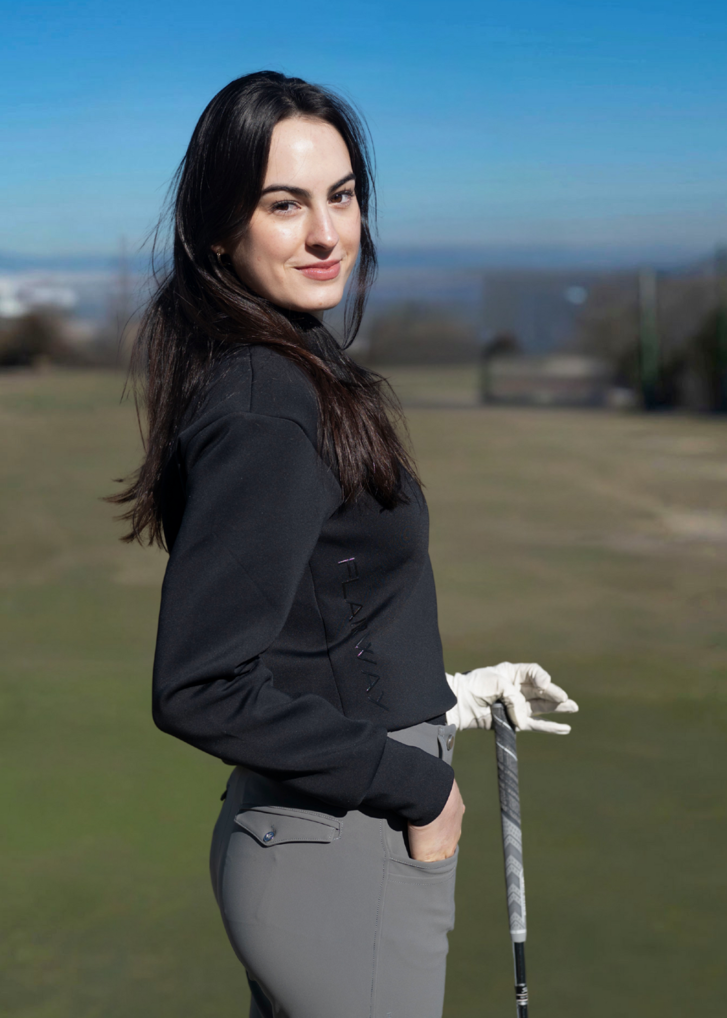 A woman wearing a navy-colored sweater with an athletic fit, featuring a quarter-zip design and a collar. The sweater is styled for golfing with a subtle logo on the side.