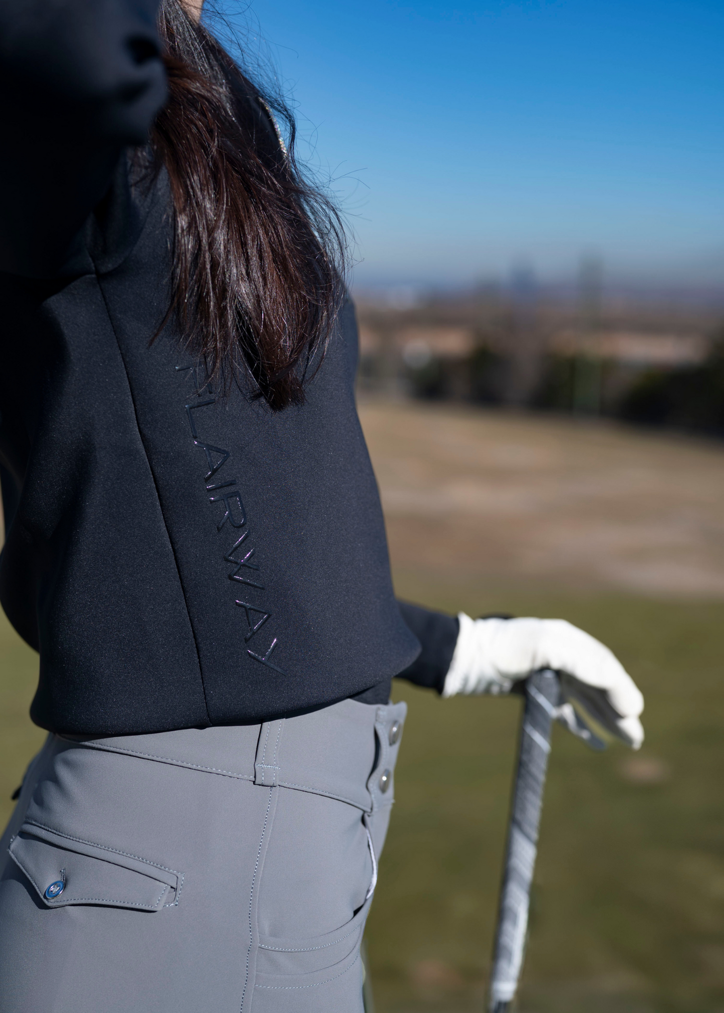 A woman wearing a navy-colored sweater with an athletic fit, featuring a quarter-zip design and a collar. The sweater is styled for golfing with a subtle logo on the side.
