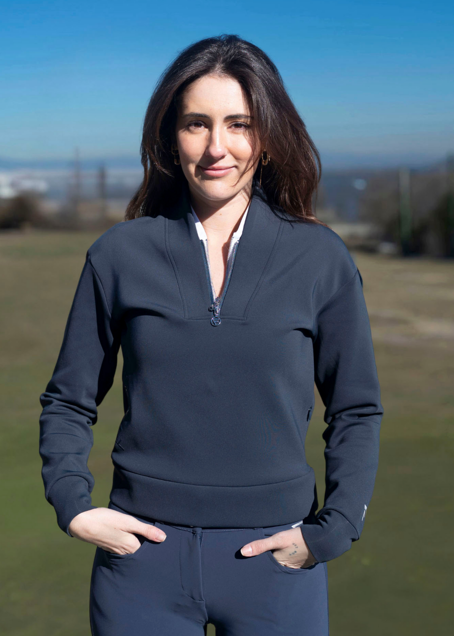 A woman wearing a navy-colored sweater with an athletic fit, featuring a quarter-zip design and a collar. The sweater is styled for golfing with a subtle logo on the side.