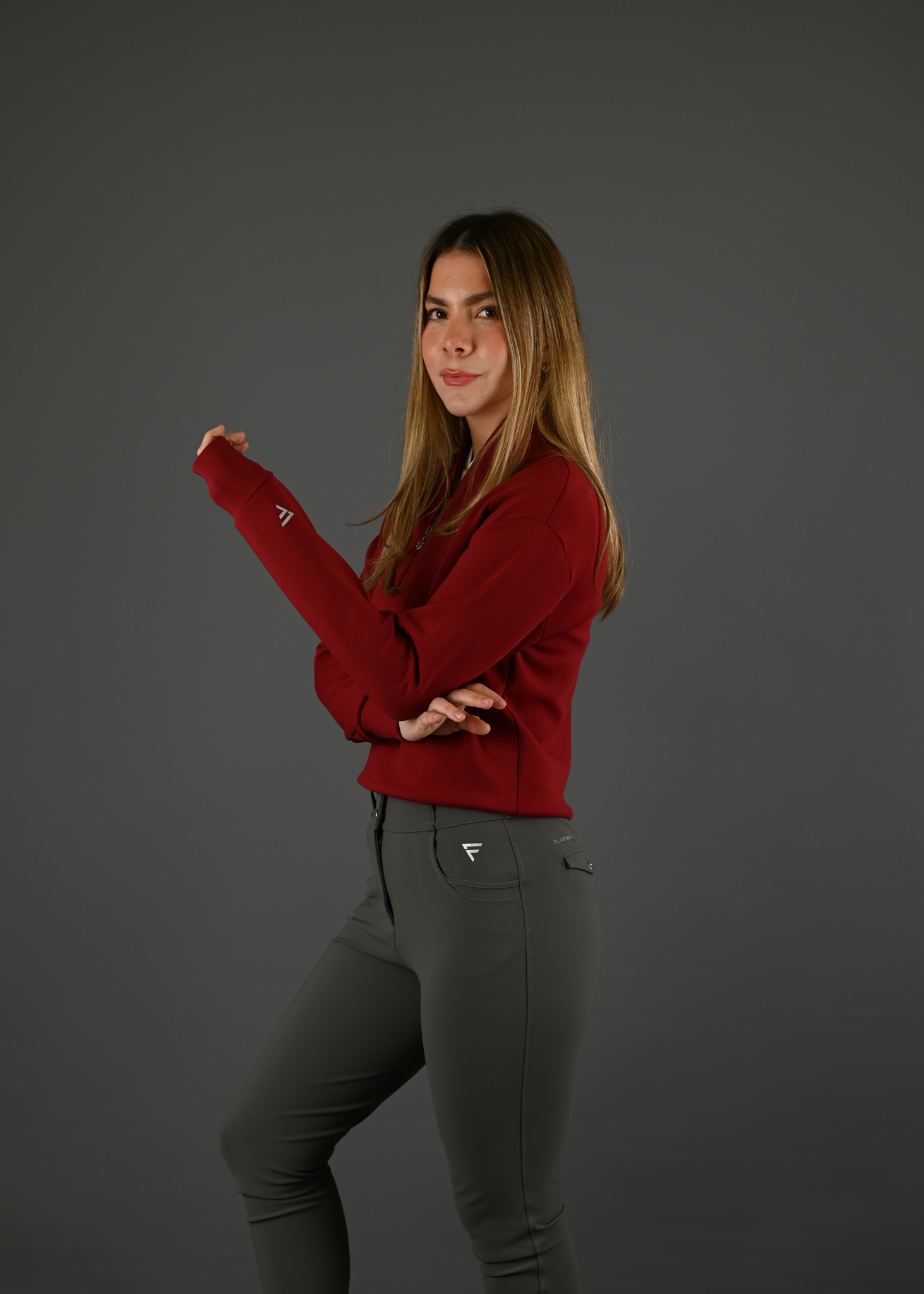 Woman wearing a red hoodie and gray pants on a dark background