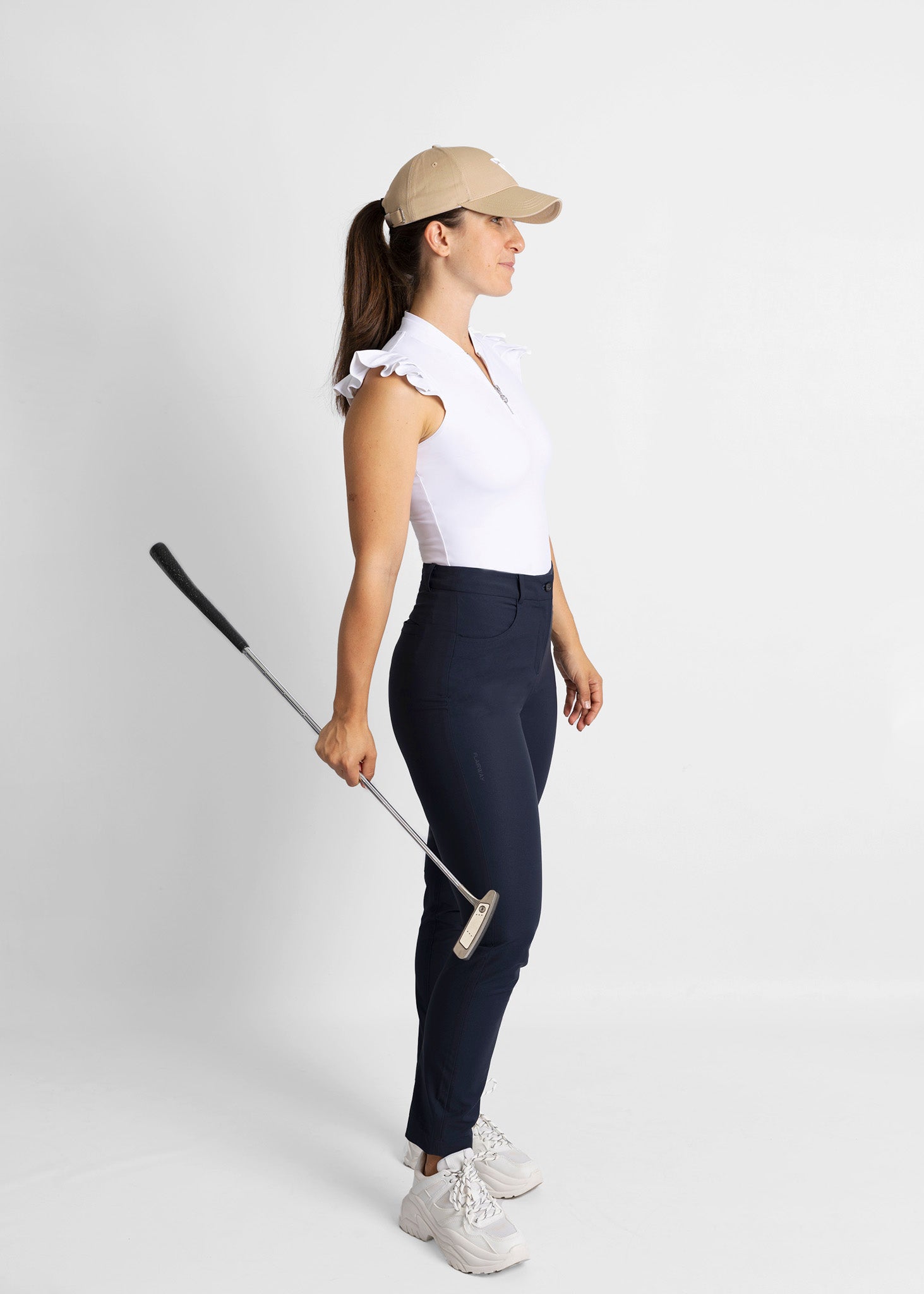 unisex organic cotton golf cap (beige) featured with high-waisted golf pants (navy) and sleeveless golf shirt with ruffle details (white)